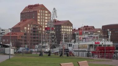 HELSINKI, FINLAND - 12 Aralık 2025: modern kırmızı tuğlalı apartmanlar ve Hietalahti limanındaki tarihi tersane vinci. Restoran teknesi bulutlu bir kış gününde rıhtıma yanaştı..