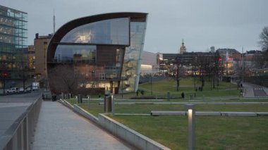 HELSINKI, FINLAND - 12 Aralık 2025: alacakaranlıkta Kiasma Müzesi. İnsanlar parkta arka planda Bio Rex neon ışıklarıyla yürür..