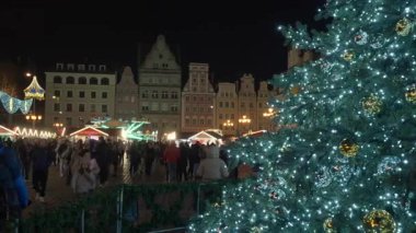 Polonya 'nın Wroclaw kentinde gece büyük dekore edilmiş Noel ağacı şenlik pazarının önünde duruyor. Kış kutlamaları sırasında insanlar tatil tezgahları ve tarihi binaların arasında yürüyorlar..