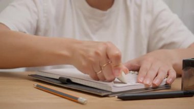 Tahta masadaki sarmal defterdeki hataları silmek için beyaz silgi kullanan kadın eli. Hataları düzeltme, metni düzenleme ya da çalışma ya da çalışma sırasında baştan başlama kavramı. Özgün ses dahil.