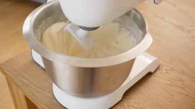 Elektrikli stand mikseri paslanmaz çelik kasedeki beyaz kremalı hamuru yener. Mutfak aletleri yüksek hızda çalışır ve yüksek sesli motor sesiyle kremalı kek yapar. Pişirme hazırlığı yakın plan.