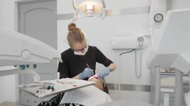 Profesyonel kadın dişçi, diş ısırığı tıkanıklığını kontrol etmek ve modern stomatoloji kliniğinde yeni dolgu ayarlamak için hasta ağzına eklemli kağıt koymak için cımbız kullanır..