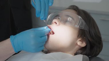 Doktor iğneden önce lokal anestezi jeliyle pediatrik hasta oral mukozasını temizliyor. Çocuk, profesyonel stomatoloji dolabında acısız diş tedavisi için hazırlanıyor..