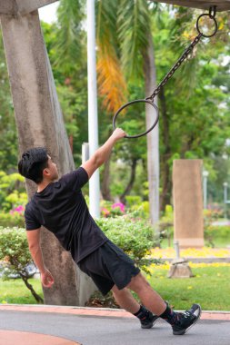 Genç adam parkta demir halkayla egzersiz yapıyor.