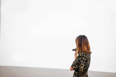 Asyalı kadın boş ekranda mikrofonla konuşuyor.