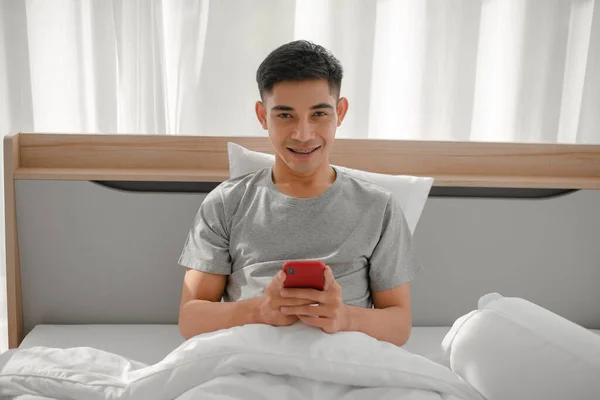 Young asian guy smile on the bed with smartphone