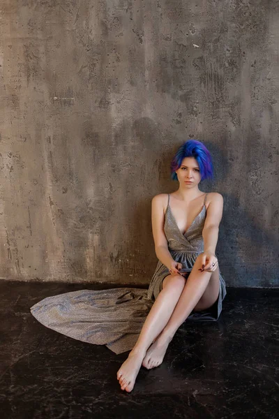 model with blue hair in a silver dress against the wall