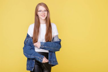 Şeffaf gözlüklü ve sarı arka planda mavi kot ceketli bir kız.