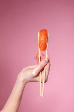 Pembe arka planda elinde somon balığı olan bir suşi.