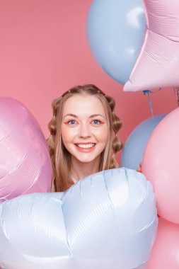 Pembe arka planda balonları olan parlak makyajlı bir kadın.