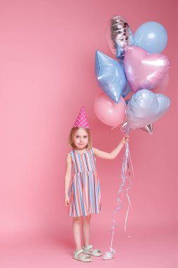 Küçük kız kafasında şapkayla ve doğum gününde balonlarla