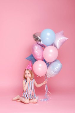 Şapkalı küçük kız bir sürü balonla oturuyor.