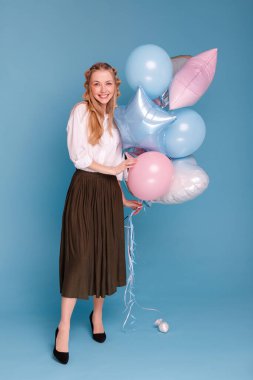 Mavi arka planda balonları olan çekici güzel bir kadın.