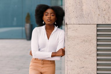 Gri duvarın yanında bukleleri olan koyu tenli kadın.