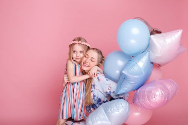 Anne ve kızı pembe stüdyo arka planında balonlarla sarılıyorlar.