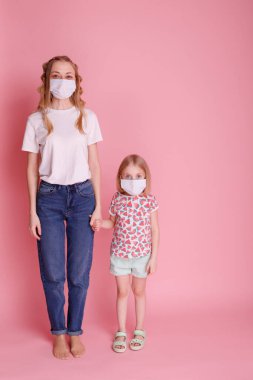 Anne ve kız tıbbi maskeli pembe arka planda yüzleri var.