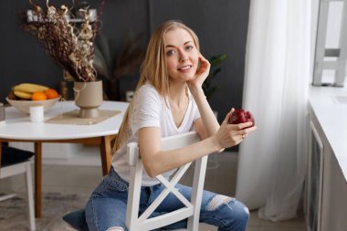 Evde sandalyesinde elma olan çekici bir sarışın.