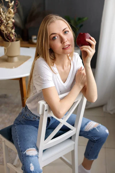 woman blonde with red apple on a chair near the table