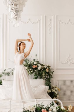 Beyaz elbiseli dansçı. Yatağın üzerinde çiçekler var.