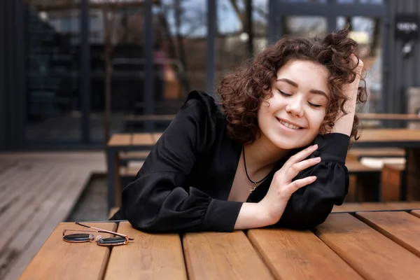 Glücklich Gelocktes Mädchen Schwarzer Jacke Lächelt Und Sitzt Einem Holztisch — Stockfoto