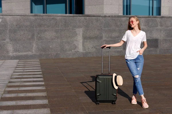 Beyaz tişörtlü ve kot pantolonlu bir kadın. Yaz tatilinde bavullu.