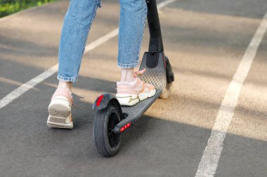 Elektronik scooter ve yazın şehir parkında yürüyüş yapan bir kız. yakın plan