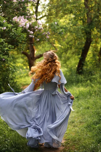 Elbiseli ve saç stili olan çekici bir kadın yaz bahçesinde koşuyor.