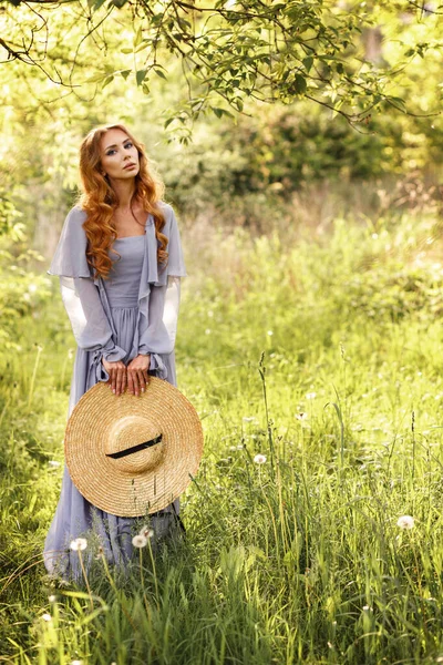 Hasır şapkalı ve leylak elbiseli bir kız yazın bahçede yürüyüş yapıyor..