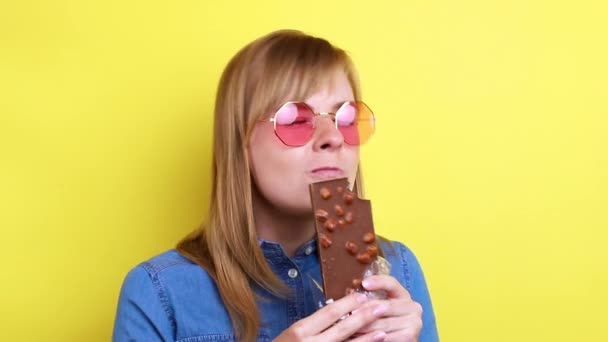 Woman Pink Glasses Eating Chocolate Yellow Background — Vídeo de Stock