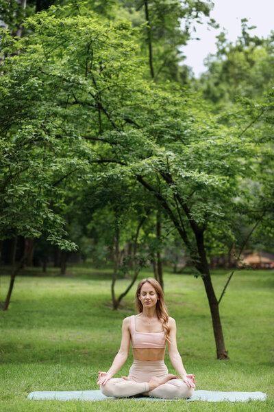 Attractive female yoga instructor in the park meditates