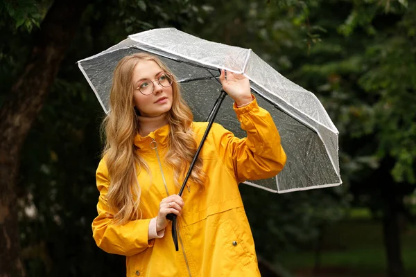 緑の背景に雨の中で傘と黄色のレインコートのブロンド — ストック写真