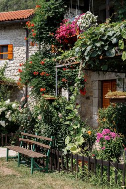 Yazlık bahçede kiremit çatılı taş bir binanın yanında bir bank. Yaz havası