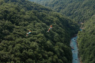 İki turist yeşil dağların ve nehirlerin arka planında bir halat hattında