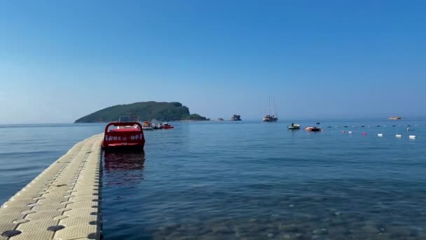 rekreační motorový člun na molu s ostrovem sv. Mikuláše v pozadí. Budva. Černá Hora 12.07.2021