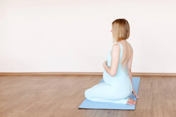 ヨガのスーツを着た妊婦がベージュの背景で瞑想するスポーツマットで — ストック写真