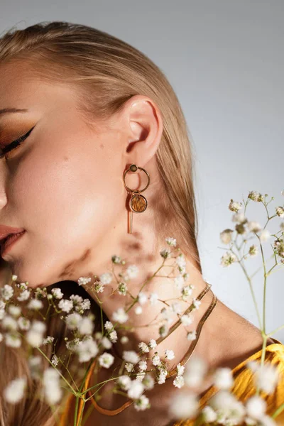 close-up of earrings on the ear of a blonde model with a bouquet of flowers. fashion blogger