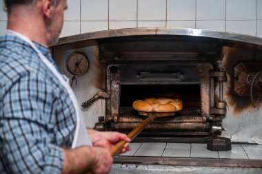 Baker, eski ahşap fırınına yeni örülmüş bir hamur koyuyor geleneksel zanaatkar ekmeği fırında pişiriyor.