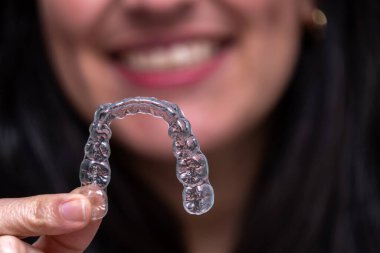 Gülümseyen bir kadın, şeffaf diş hizalayıcısını gösteriyor. Mükemmel bir gülümseme ve ağız sağlığı için modern ortodontik tedavi