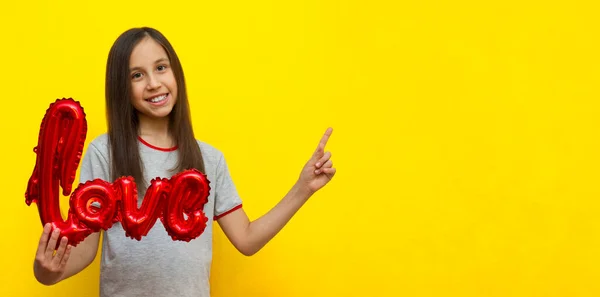 Banner. Uma menina sorridente com longos cabelos escuros em um fundo amarelo segura uma bola com a inscrição amor. — Fotografia de Stock