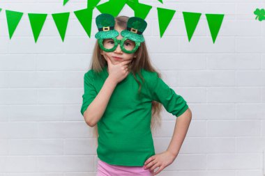 Yeşil tişörtlü, düşüncelere dalmış beyaz bir kızın portresi. Aziz Patrick Günü 'nde yeşil bayraklı beyaz leprikon gözlük takıyor..