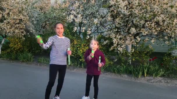 Zwei glückliche Mädchen, Schwestern im Alter von zehn und sechs Jahren, pusten im Frühling Blasen auf der Straße. — Stockvideo