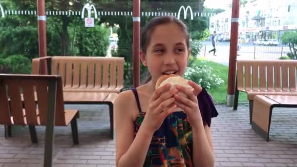 Happy smiling girl eating a cheeseburger at a McDonalds fast food restaurant. Ukraine, Zaporozhye 06.23.2021 — Stock Video