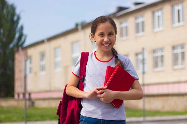 Μια χαμογελαστή έφηβη στέκεται μπροστά στο σχολείο κρατώντας βιβλία στα χέρια της. Επιστροφή στο σχολείο έννοια. Επιλεκτική εστίαση Royalty Free Εικόνες Αρχείου