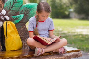 Parkta oturan düşünceli küçük kız bir kitap okuyor. Okul konseptine geri dönelim. Seçici odak