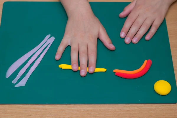 Childrens hands sculpt a figurine of a rainbow and a sun from clay on the table. View from above. — Stock Photo, Image