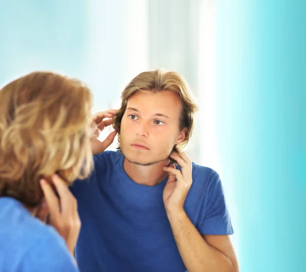 young man looking in the mirror,combing his hair,looking at problems on face