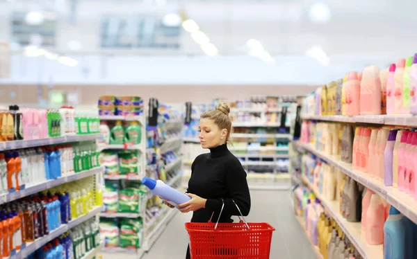 Woman shopping in supermarket reading product information.(washing powder,detergent,shampoo, soap)
