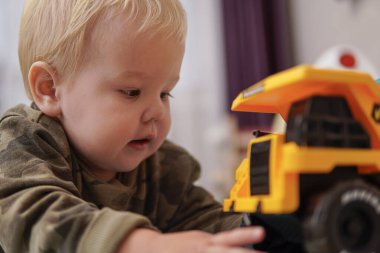 Sarı saçlı küçük çocuk yerde sarı kamyonla oynuyor. yüksek kalite