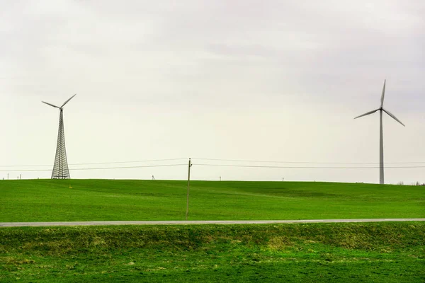 Zwei Windräder drehen sich um die Erzeugung von Energie inmitten eines Weizenfeldes. Windparks werden zu einer immer wichtigeren Quelle intermittierender erneuerbarer Energien. — Stockfoto