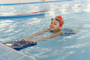 Küçük mutlu kız bilardo tahtasıyla yüzmeyi öğreniyor. Çocuklar için spor ve eğlence. Yüzme yarışması. Çocukluktan beri sağlıklı bir yaşam tarzı..